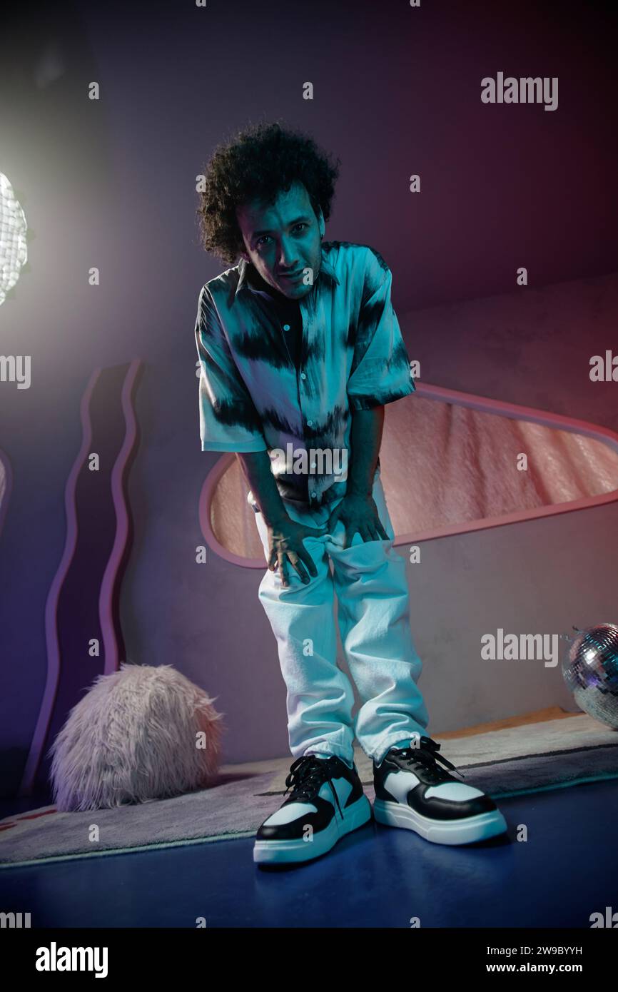 Young man standing with hands on knees looking down at camera posing in contemporary art space Stock Photo