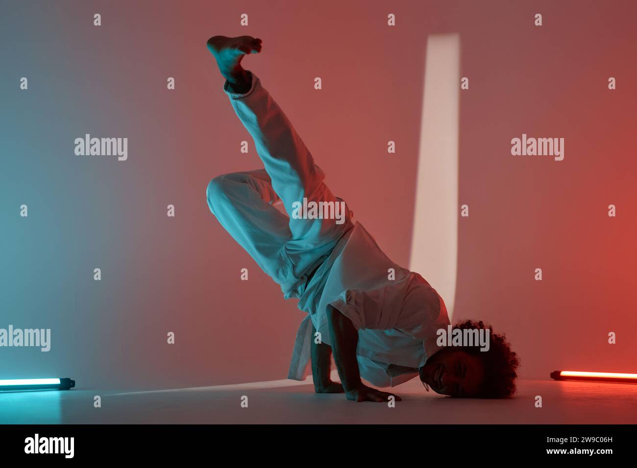 Full shot of young breakdancer doing handstand posing for camera in neon lit studio Stock Photo