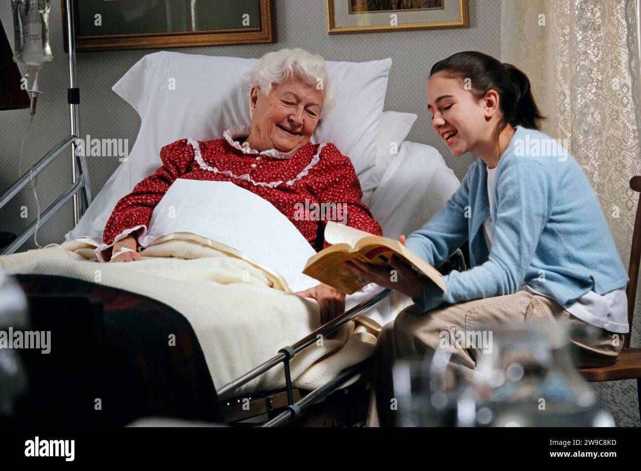 A granddaughter Reading a book to her bed ridden grandmother as she recovers at home from a medical issue Stock Photo