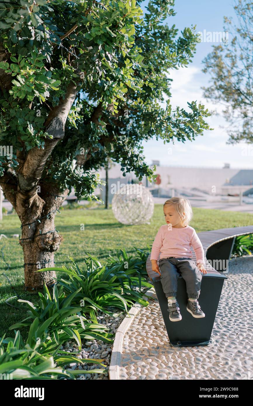 Little girl sits on a park bench and looks away Stock Photo - Alamy