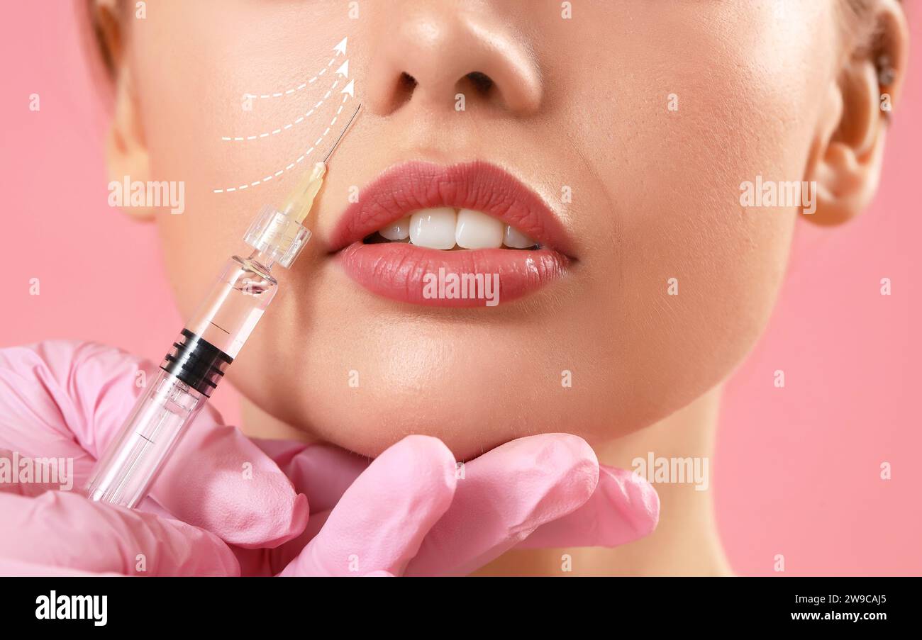 Young woman receiving filler injection in face against pink background, closeup Stock Photo