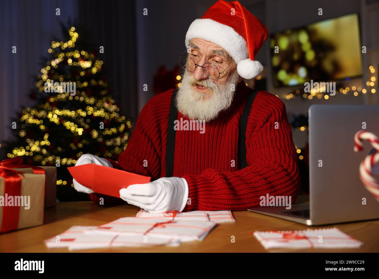 Santa Claus opening letter at his workplace in room decorated for Christmas Stock Photo