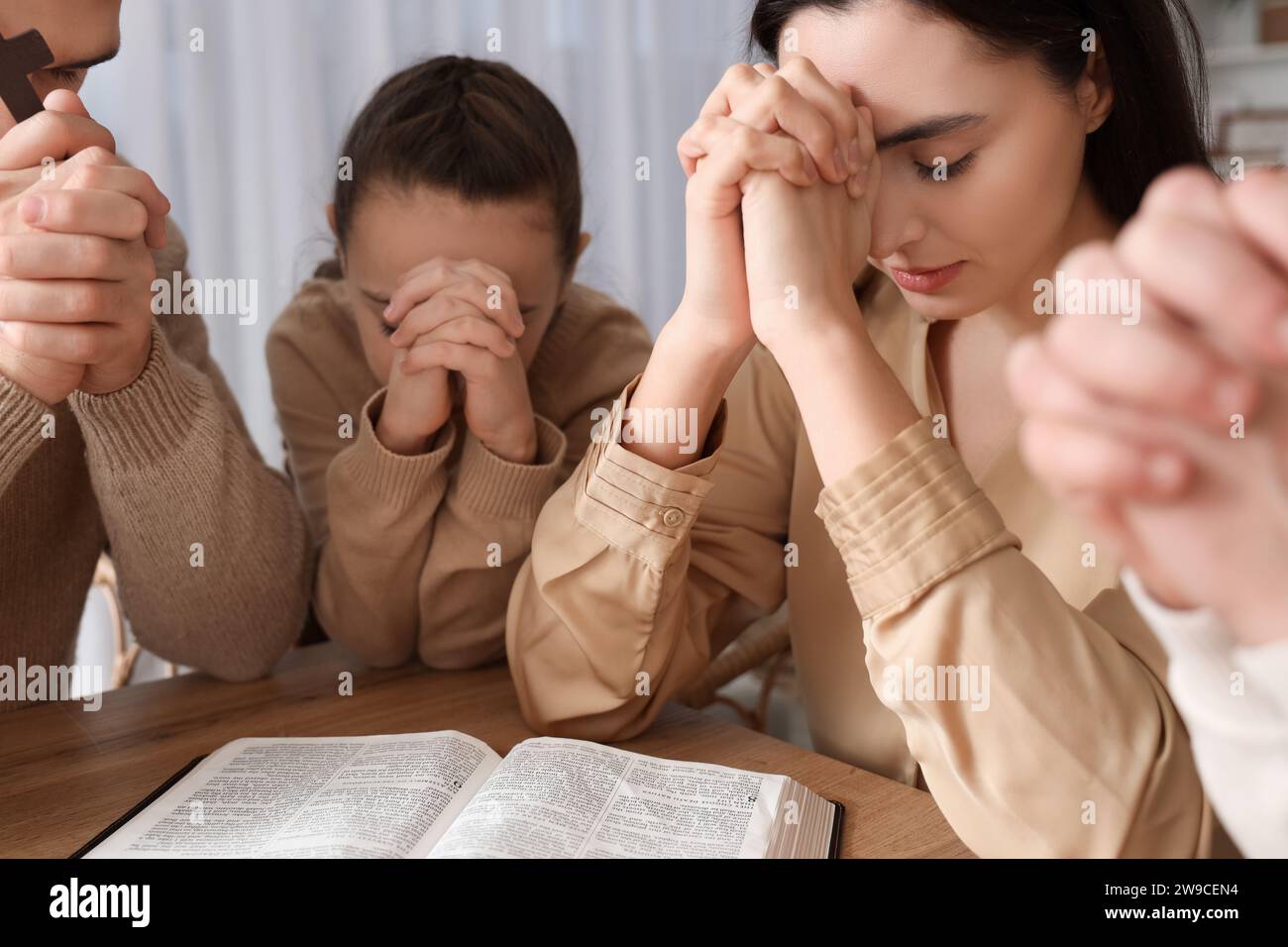Family praying together with Holy Bible on table at home Stock Photo