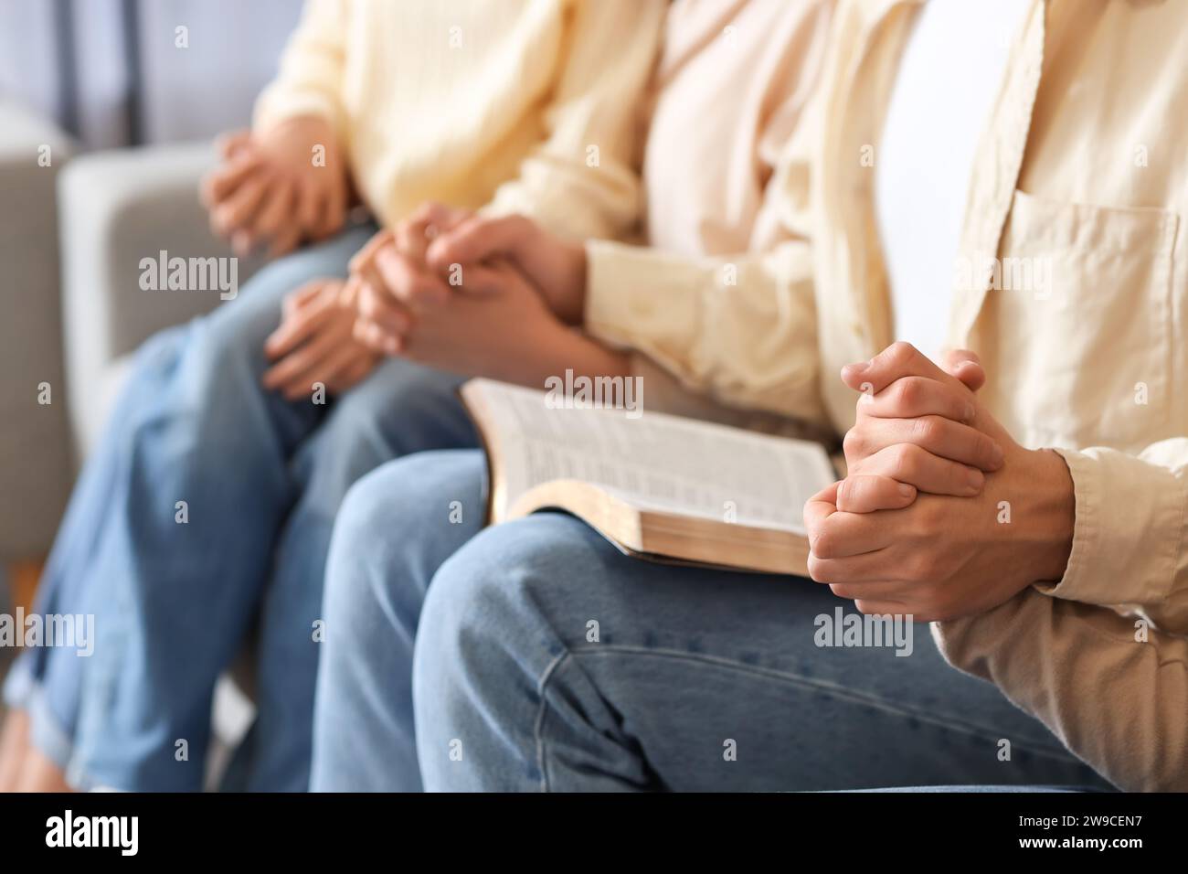 Family with Holy Bible praying on sofa at home, closeup Stock Photo