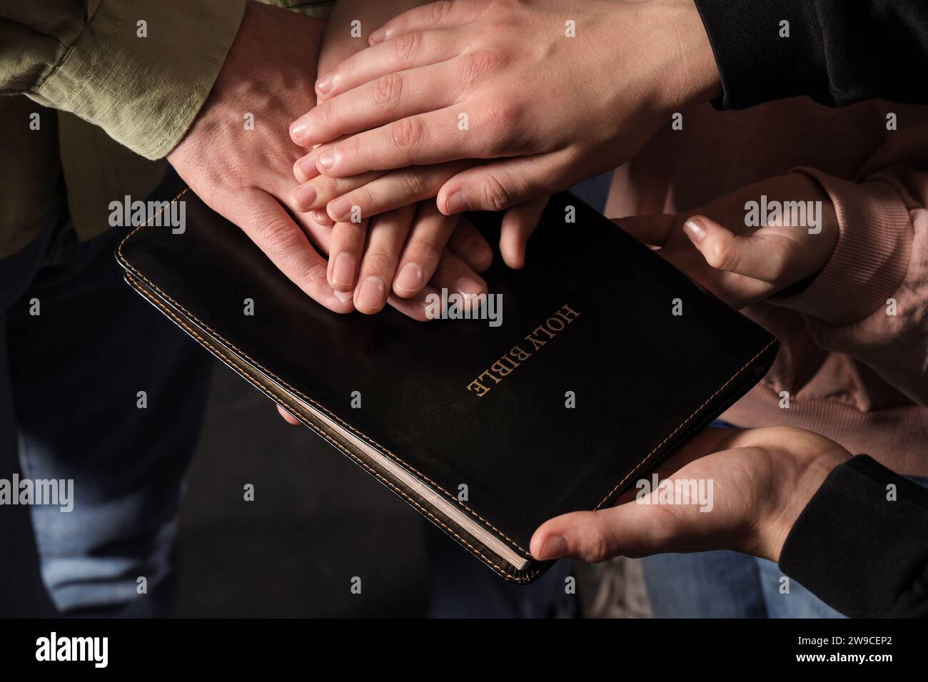 Family with Holy Bible praying together on dark background, closeup Stock Photo
