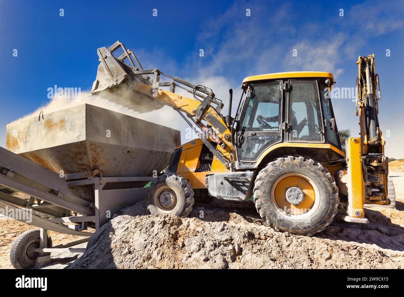 backhoe loading cement into the bin of a mixer Stock Photo