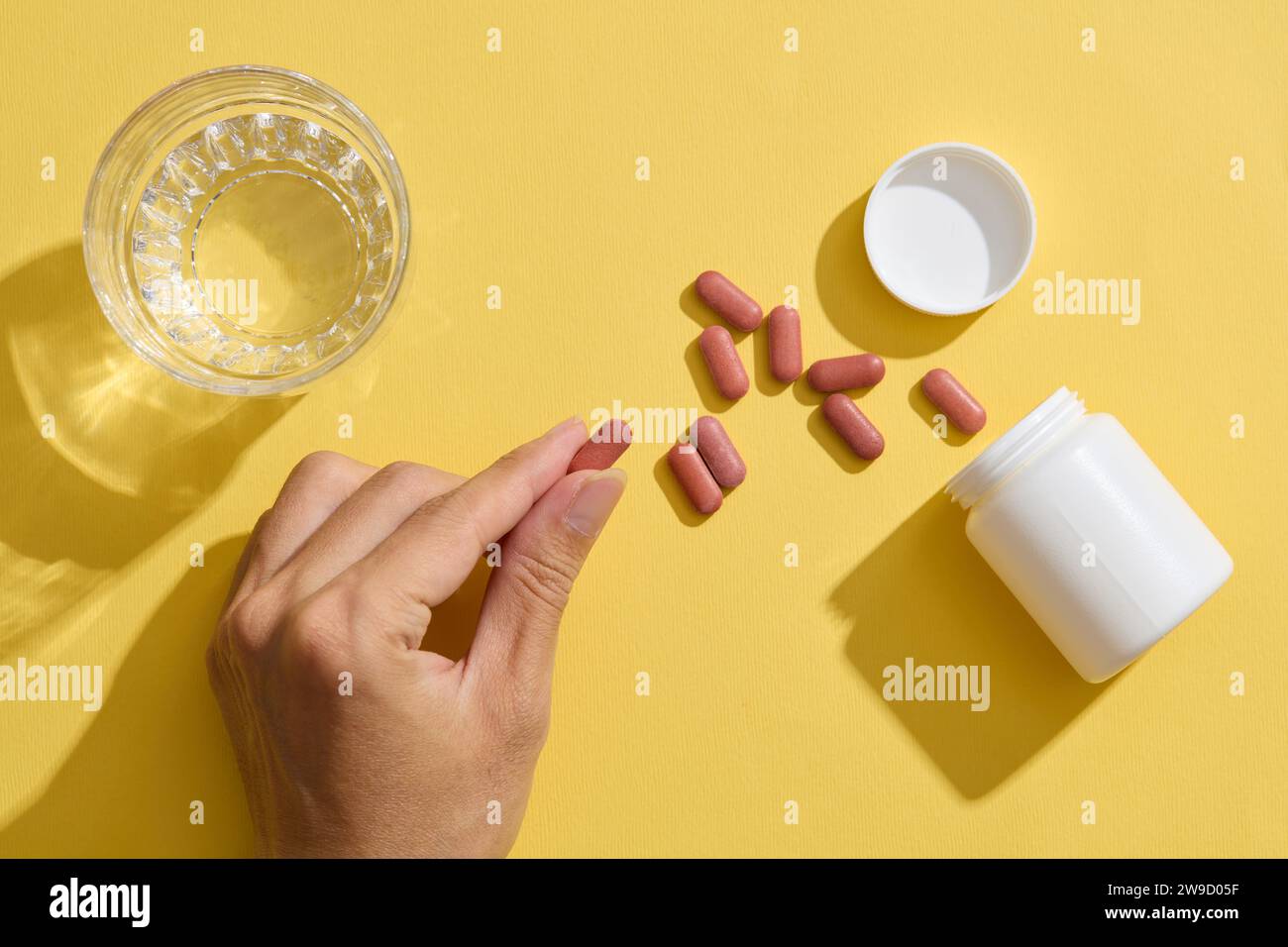 A hand holding pill, a glass of water, and an unlabeled medicine bottle