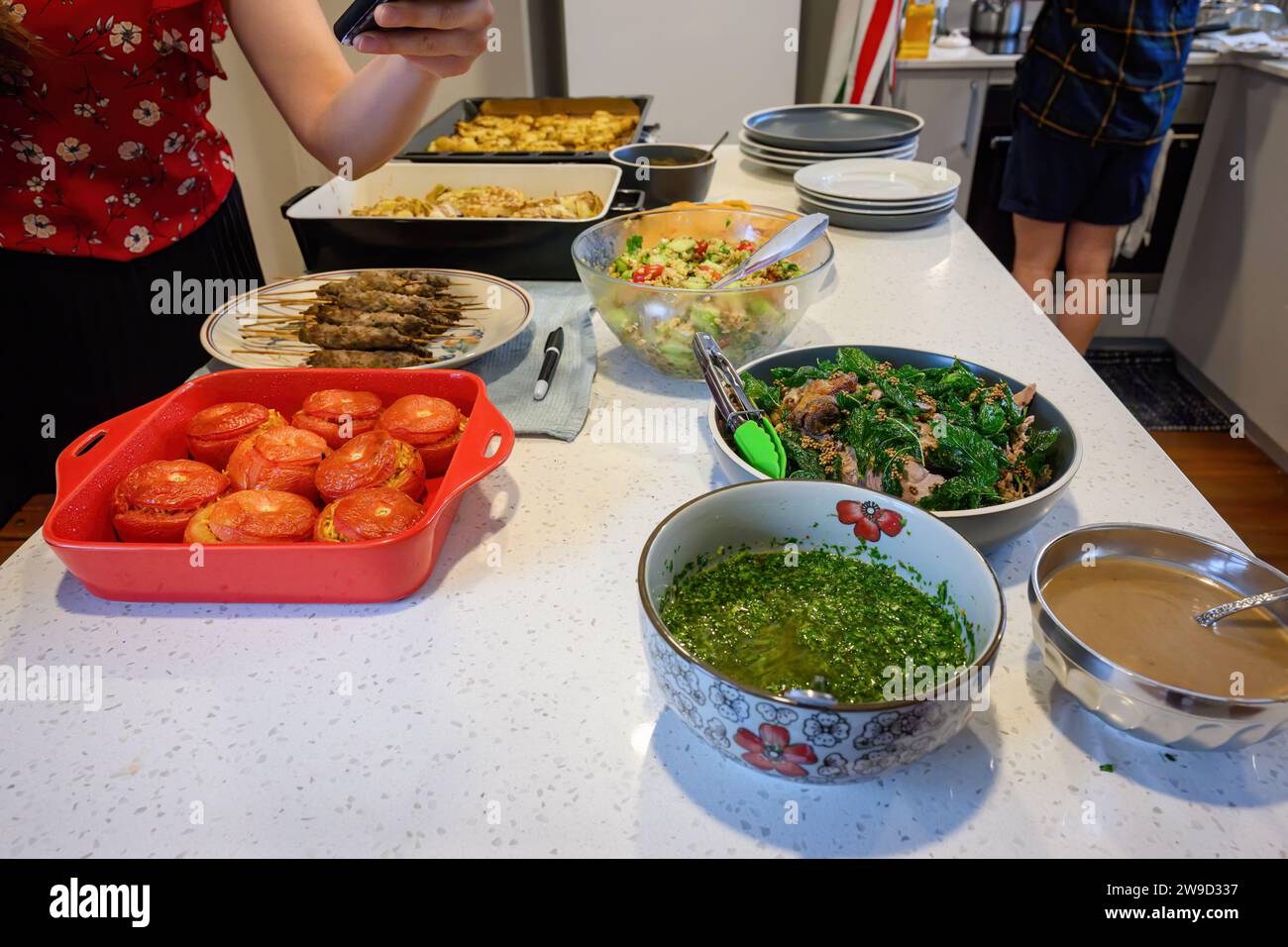 Woman holding a smartphone taking photos of festival food on the kitchen benchtop. Home cooking and entertainment concept. Stock Photo
