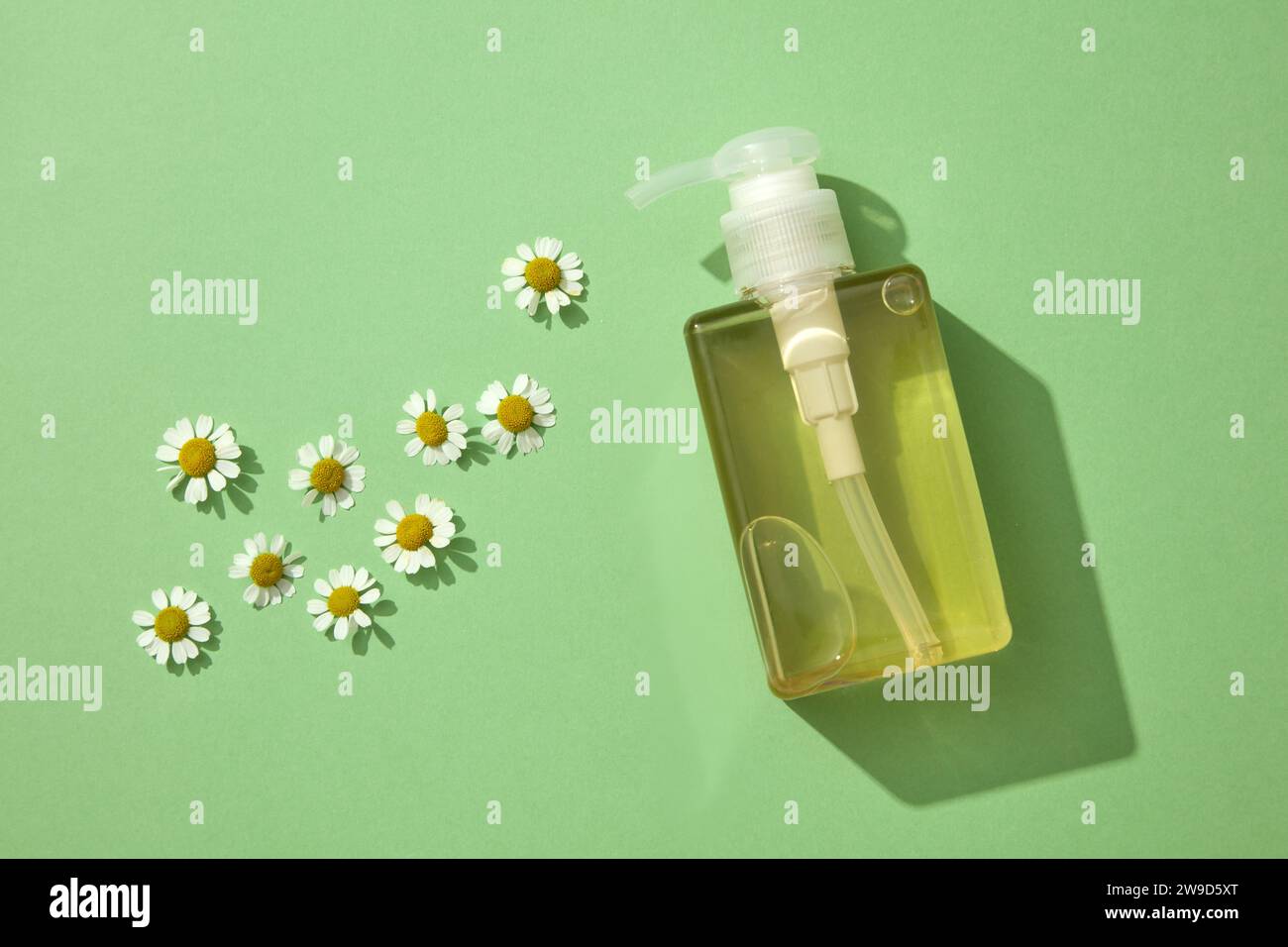 A plastic pump bottle of yellow color against a green background with fresh chamomilla flowers. Natural ingredient for cosmetics and skin care. Space Stock Photo