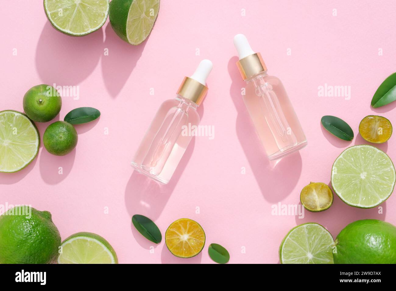 Scene for advertising cosmetic product with ingredient from natural. Kumquat and lime slices decorated with glass dropper bottles on a pink background Stock Photo
