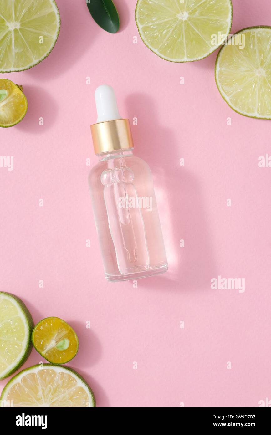 A glass dropper bottle without label decorated with slices of lime and kumquat on a pink background. Mockup scene for advertising with natural extract Stock Photo