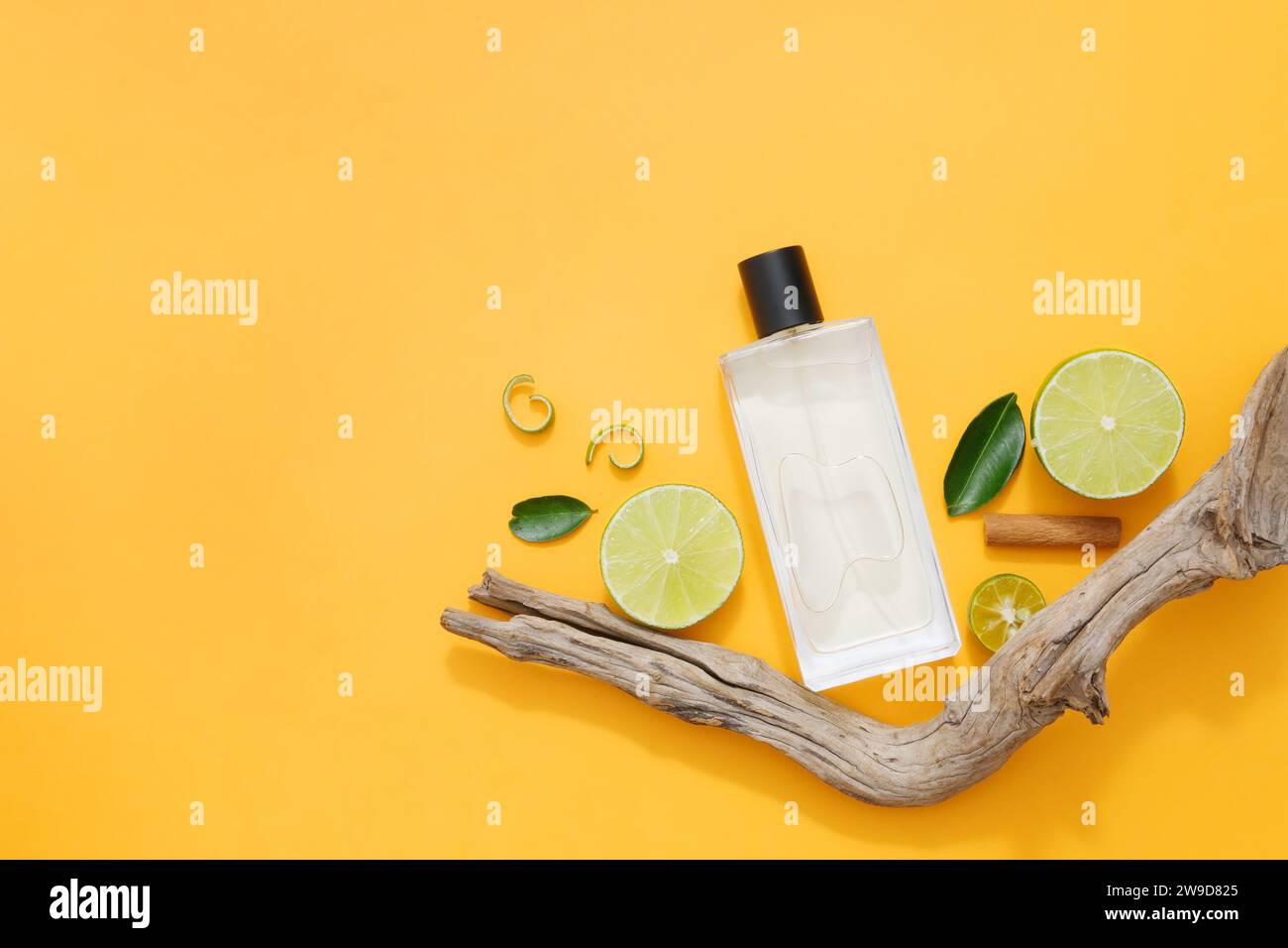 A glass perfume bottle displayed on orange background with halves of lime, green leaves and dry twig. Mockup bottle for design packaging. Copy space Stock Photo