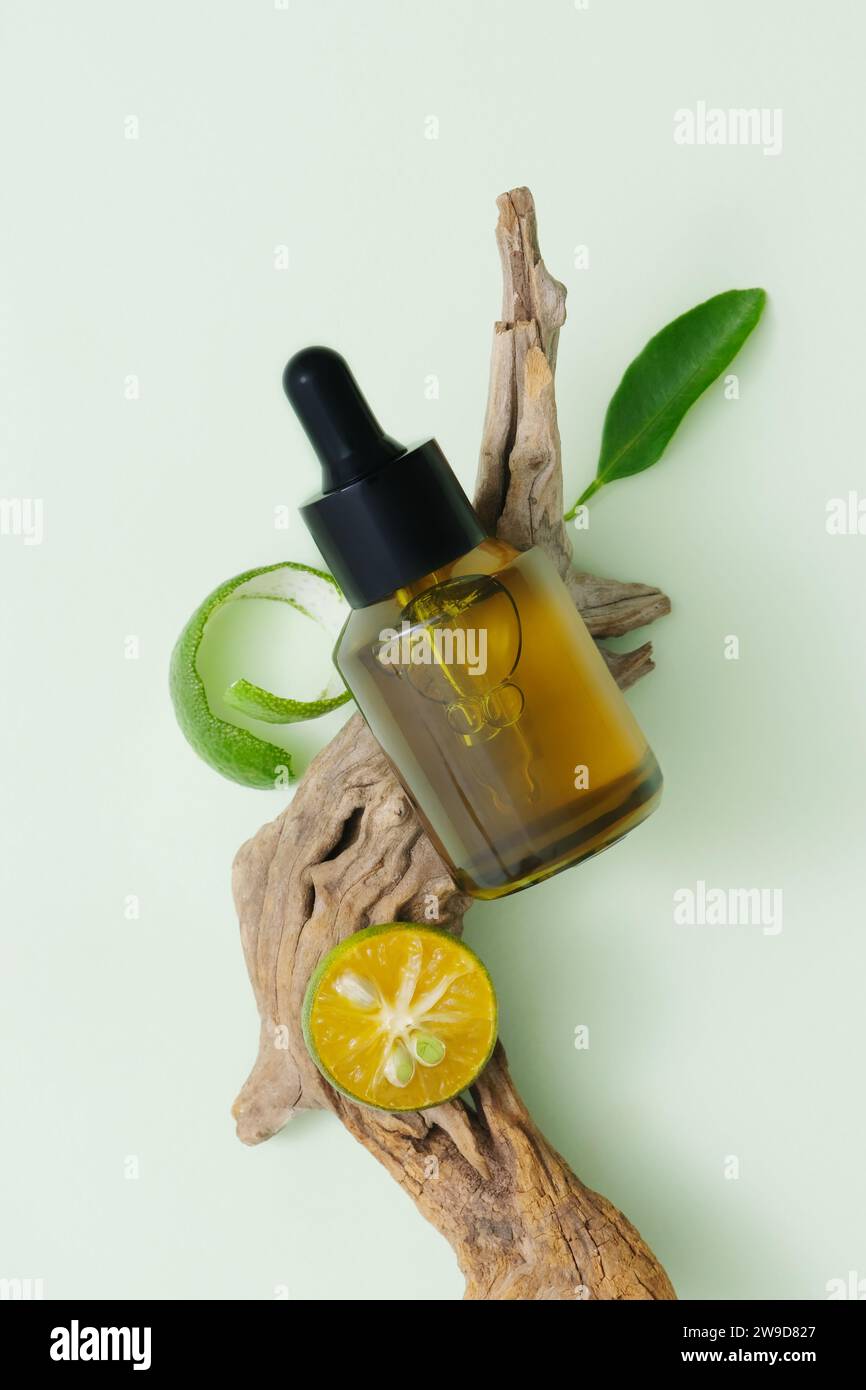 Concept of natural cosmetics with lime extract. A dropper bottle unbranded displayed on dry twig with kumquat slice and leaf. Top view, minimalist con Stock Photo