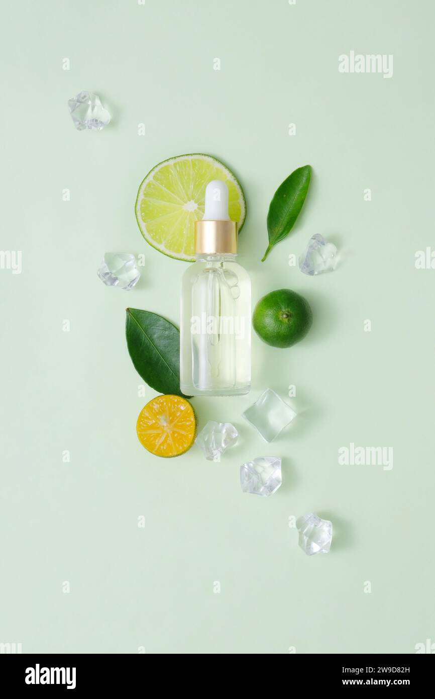 Template cosmetic mockup with glass dropper bottle decorated with kumquat, lime, green leaves and ices on pastel background. Cosmetics concept with na Stock Photo