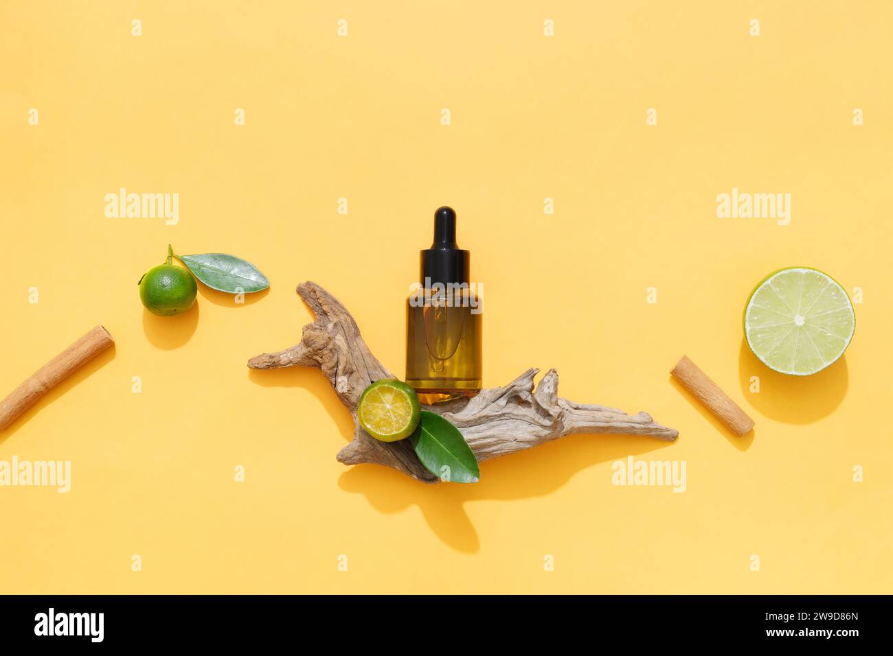 An amber serum bottle displayed on orange background with some natural ingredients: lime, kumquat and cinnamon stick. Their essential oils help improv Stock Photo
