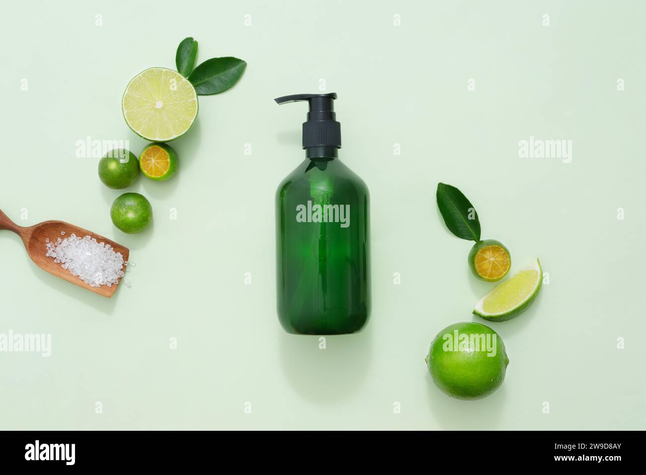 A pump bottle container shampoo or shower gel decorated with slices of lime and kumquat, green leaves and wooden tray of bath salt on green pastel bac Stock Photo