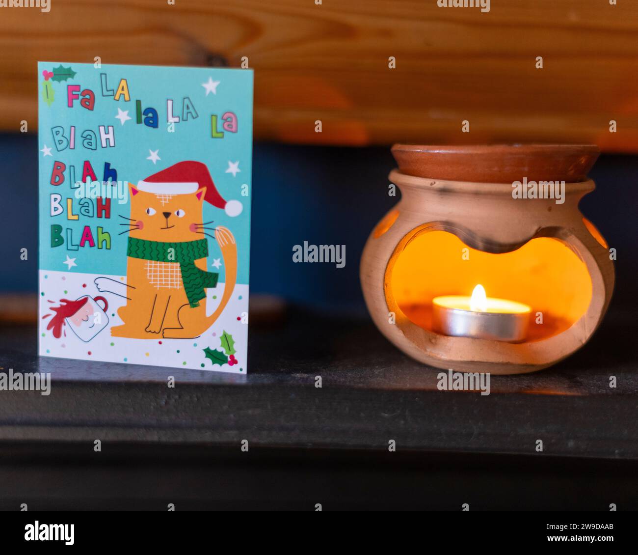 A small tea light style candle in an oil burner next to a Christmas card on a shelf in a house in the UK Stock Photo