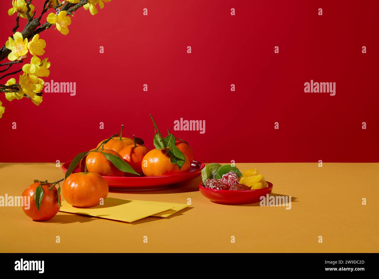 Some tangerines placed on a dish arranged with a dish of dried candy