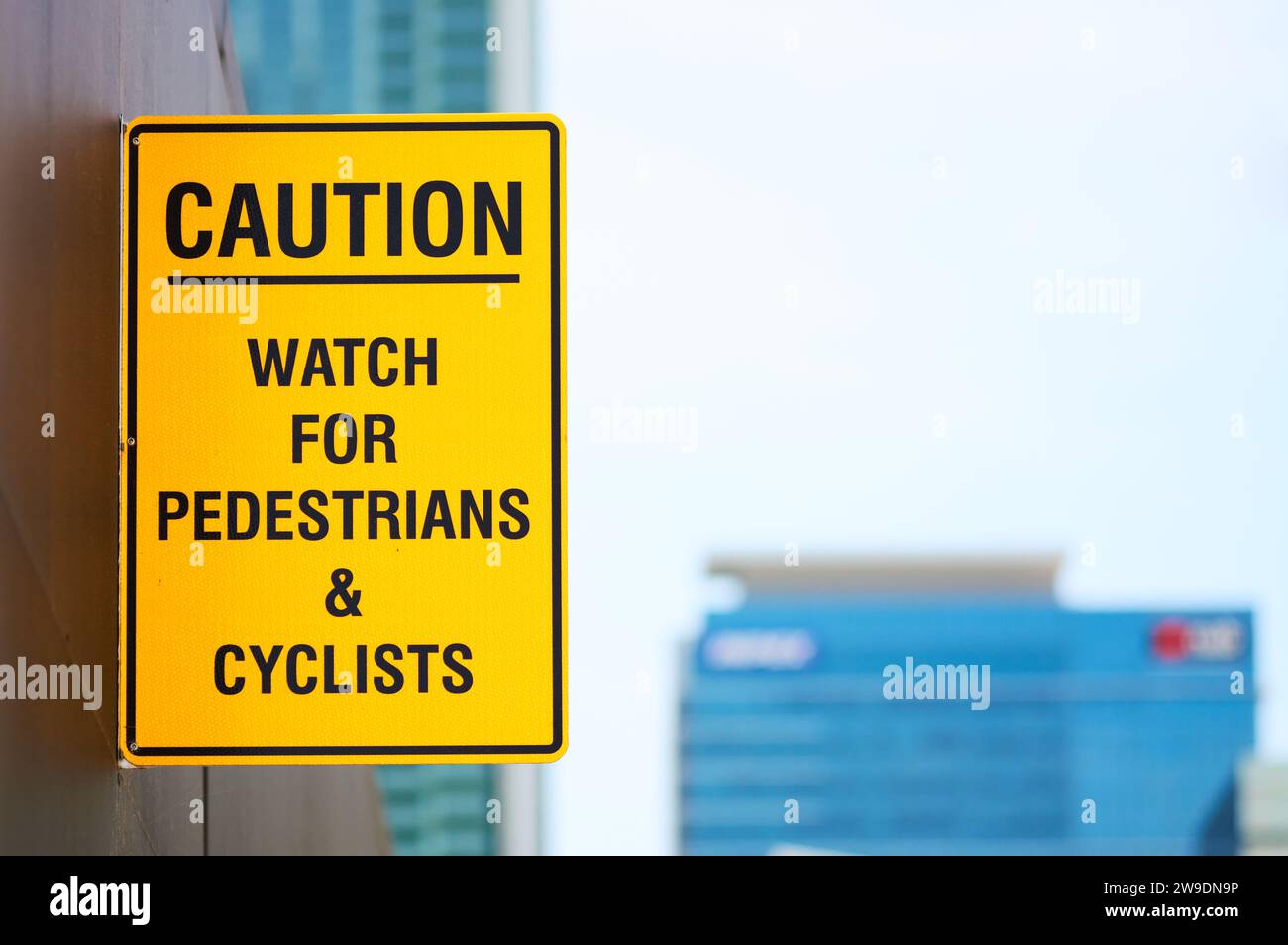 A yellow sign warning Caution, Watch for Pedestrians and Cyclists, in an urban environment with copy space. Stock Photo
