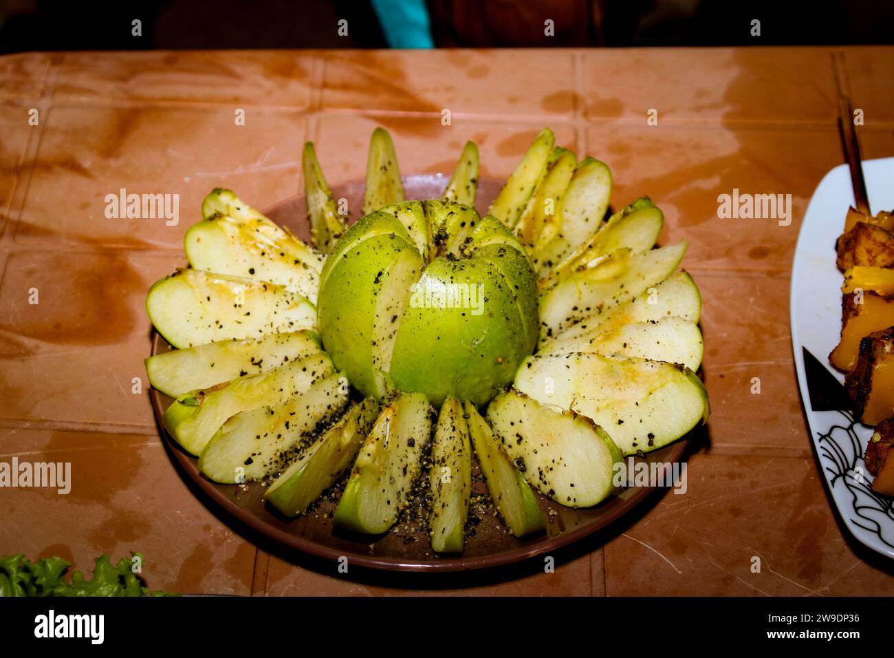 Green apple with pepper cut into pieces, lying on the saucer on a wooden background, studio lighting Stock Photo