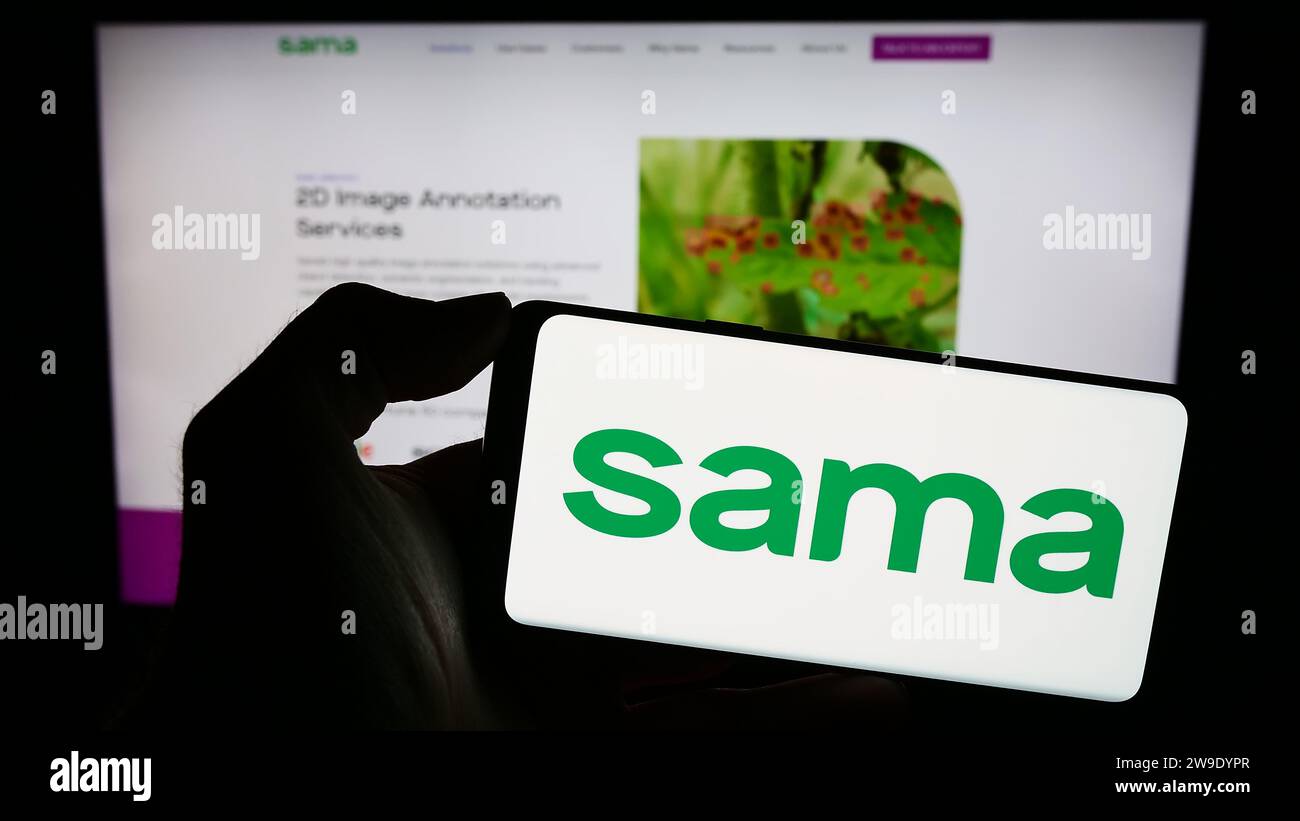 Person holding cellphone with logo of US company Samasource Impact Sourcing Inc. (Sama) in front of business webpage. Focus on phone display. Stock Photo