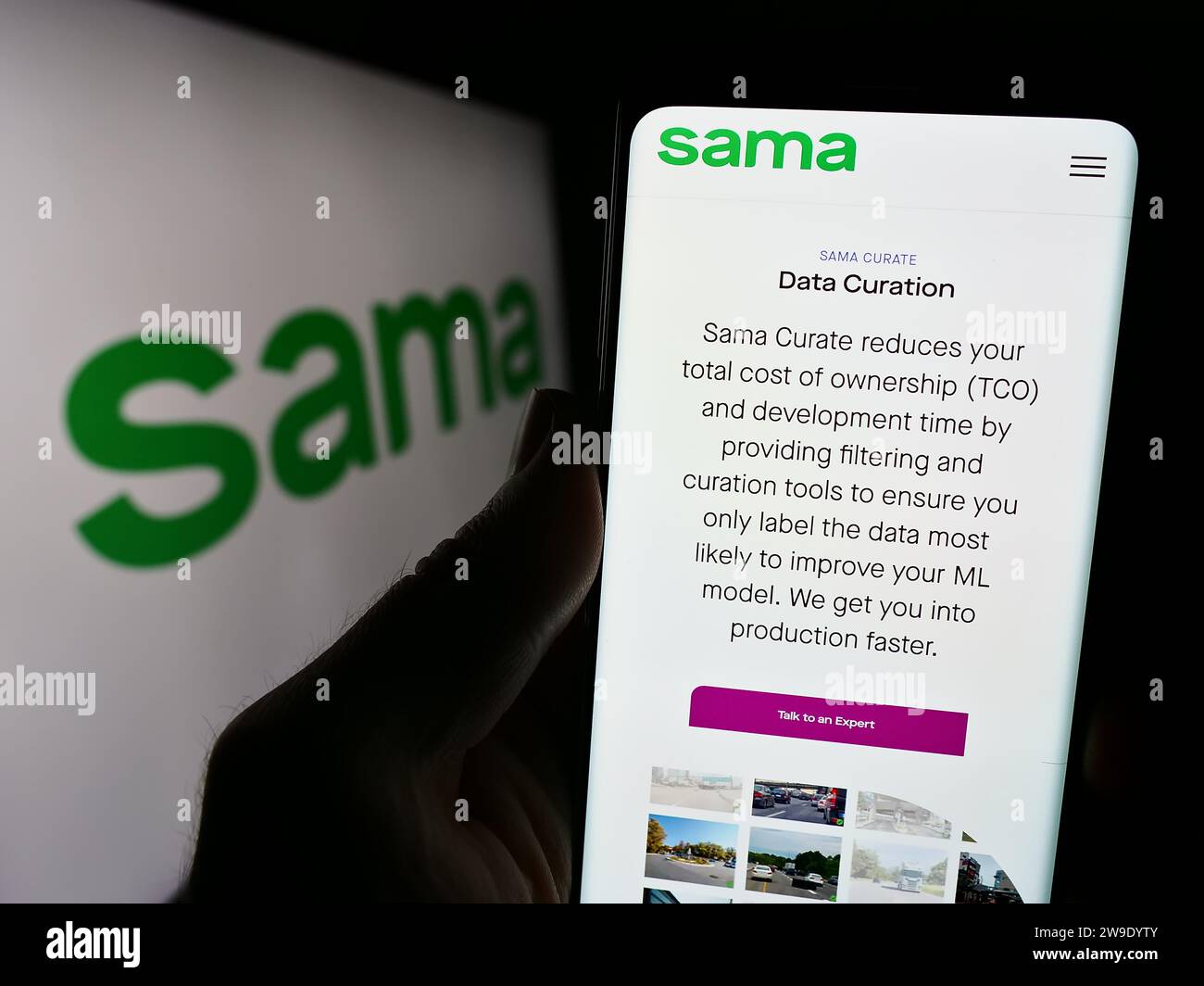 Person holding cellphone with webpage of US company Samasource Impact Sourcing Inc. (Sama) in front of logo. Focus on center of phone display. Stock Photo
