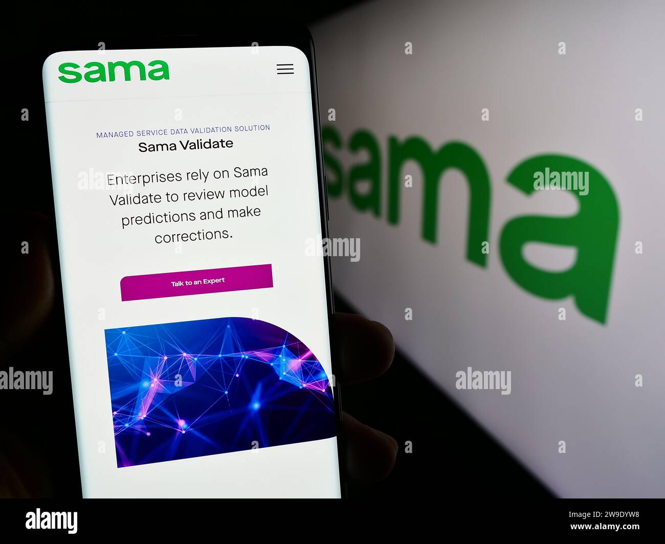 Person holding smartphone with web page of US company Samasource Impact Sourcing Inc. (Sama) in front of logo. Focus on center of phone display. Stock Photo