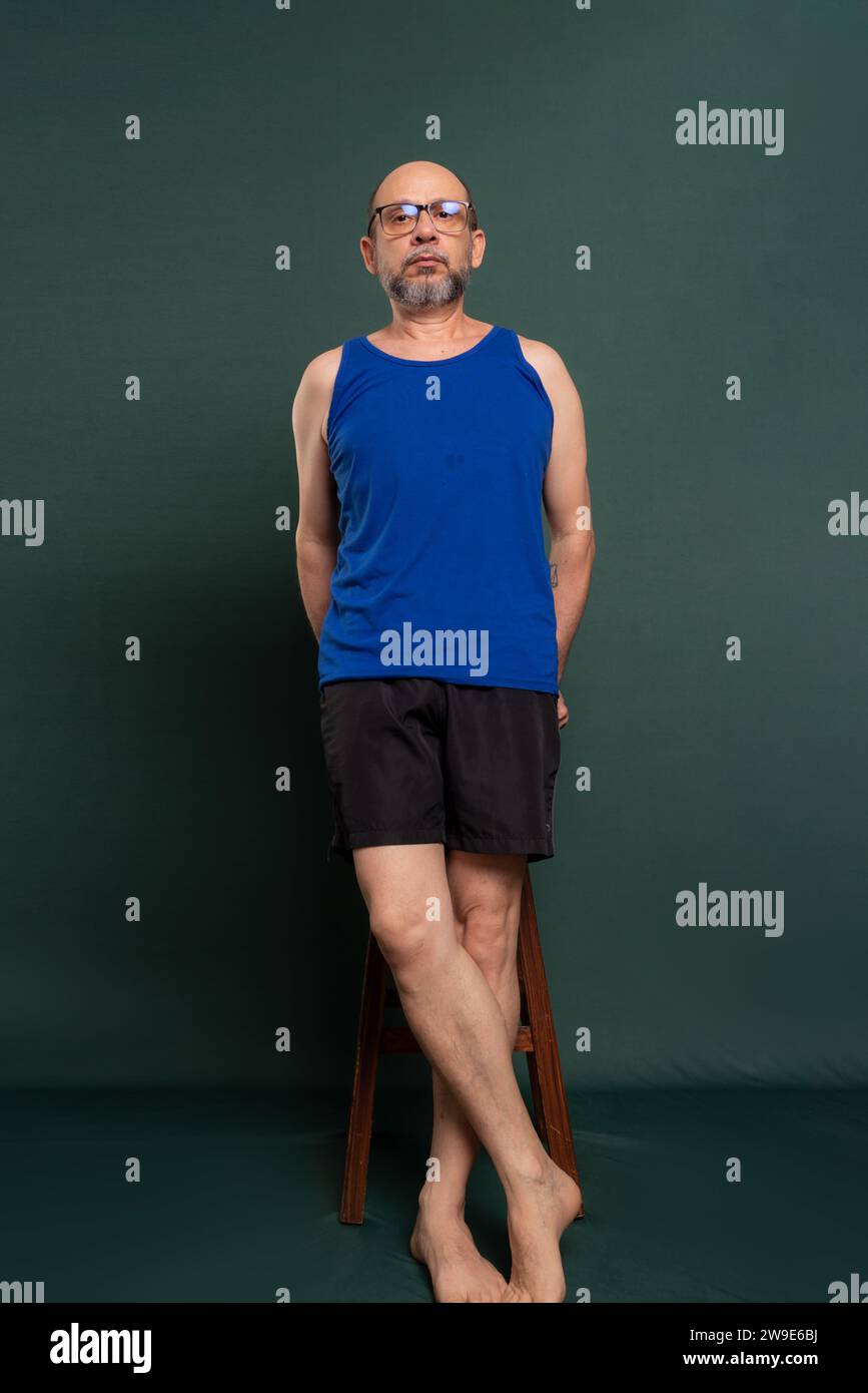 White man in a blue shirt and black shorts, standing, posing for a photo against a dark green background. Stock Photo