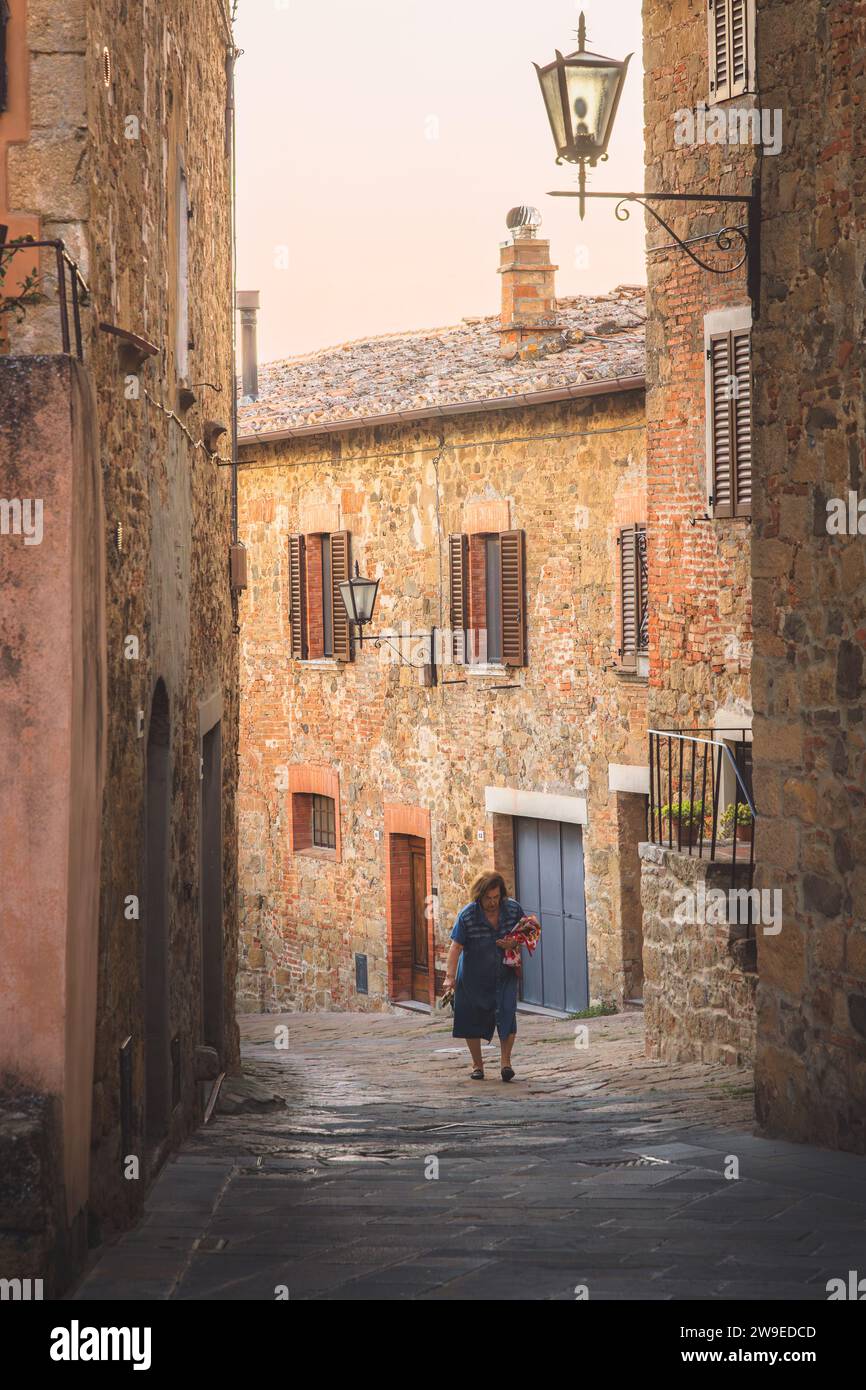 Monticchiello, Italy - August 31, 2023: A local elderly Italian woman strolls through a charming and quaint narrow old town backstreet in the historic Stock Photo