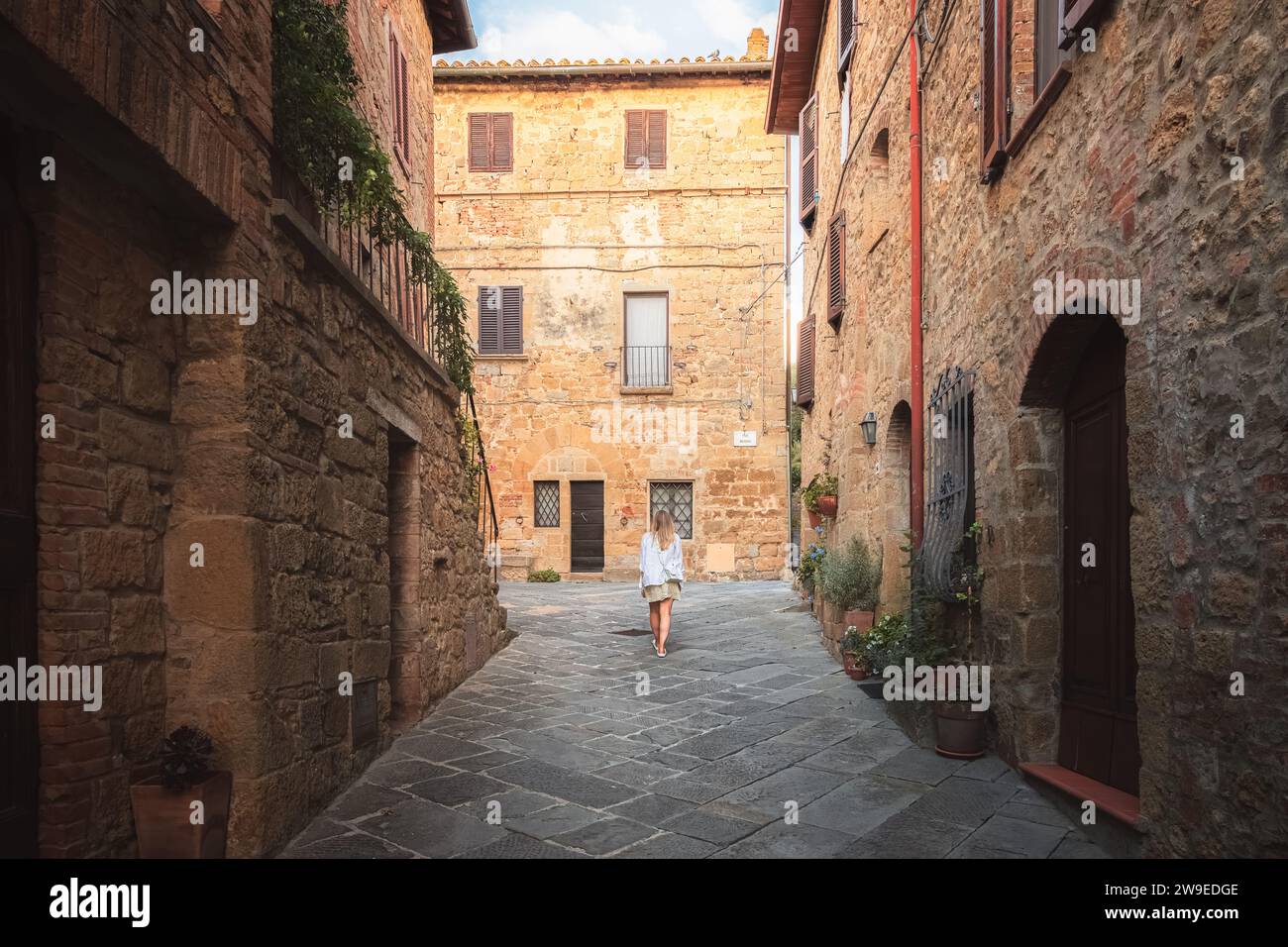 A young blonde female tourist explores backstreets of the quaint and charming Tuscan village Monticchiello, Tuscany, Italy. Stock Photo