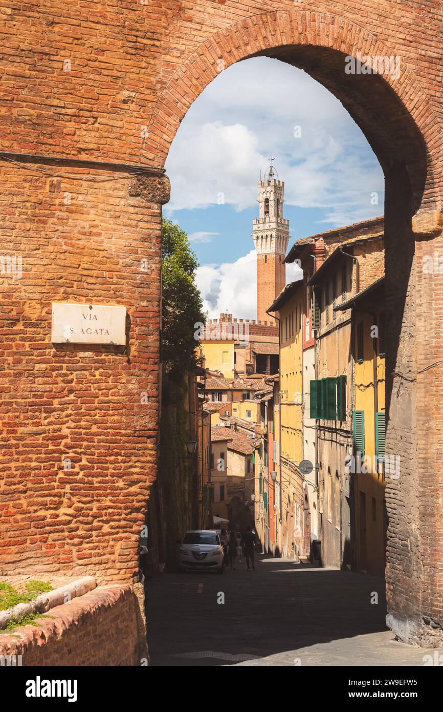 Old town entrance archway to a scenic townscape view of Torre del Mangia bell tower in the historic hilltop village of Siena, Tuscany, Italy. Stock Photo