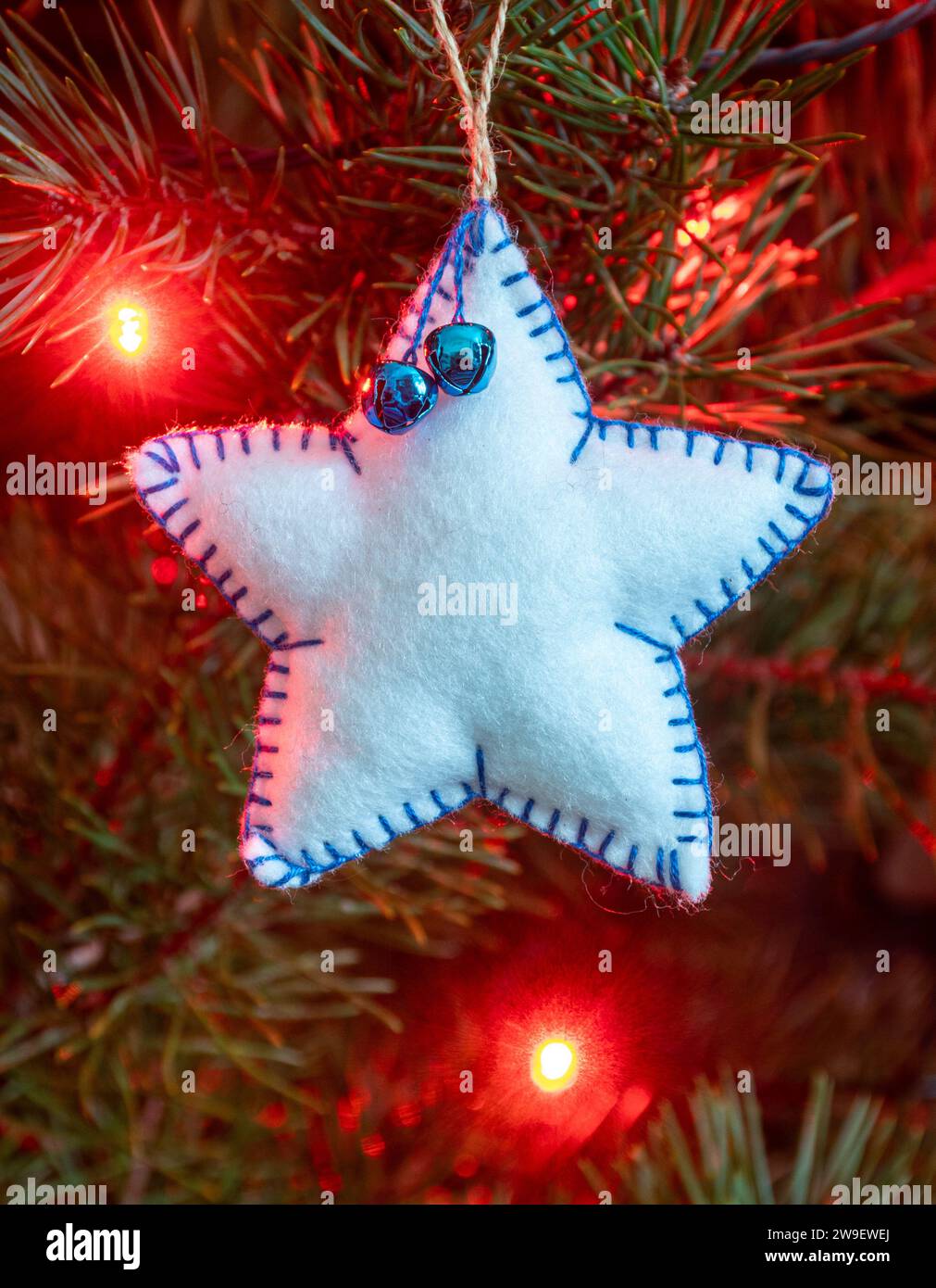 Homemade handicraft felt Christmas tree decorations on a tree with lights, a white star Stock Photo