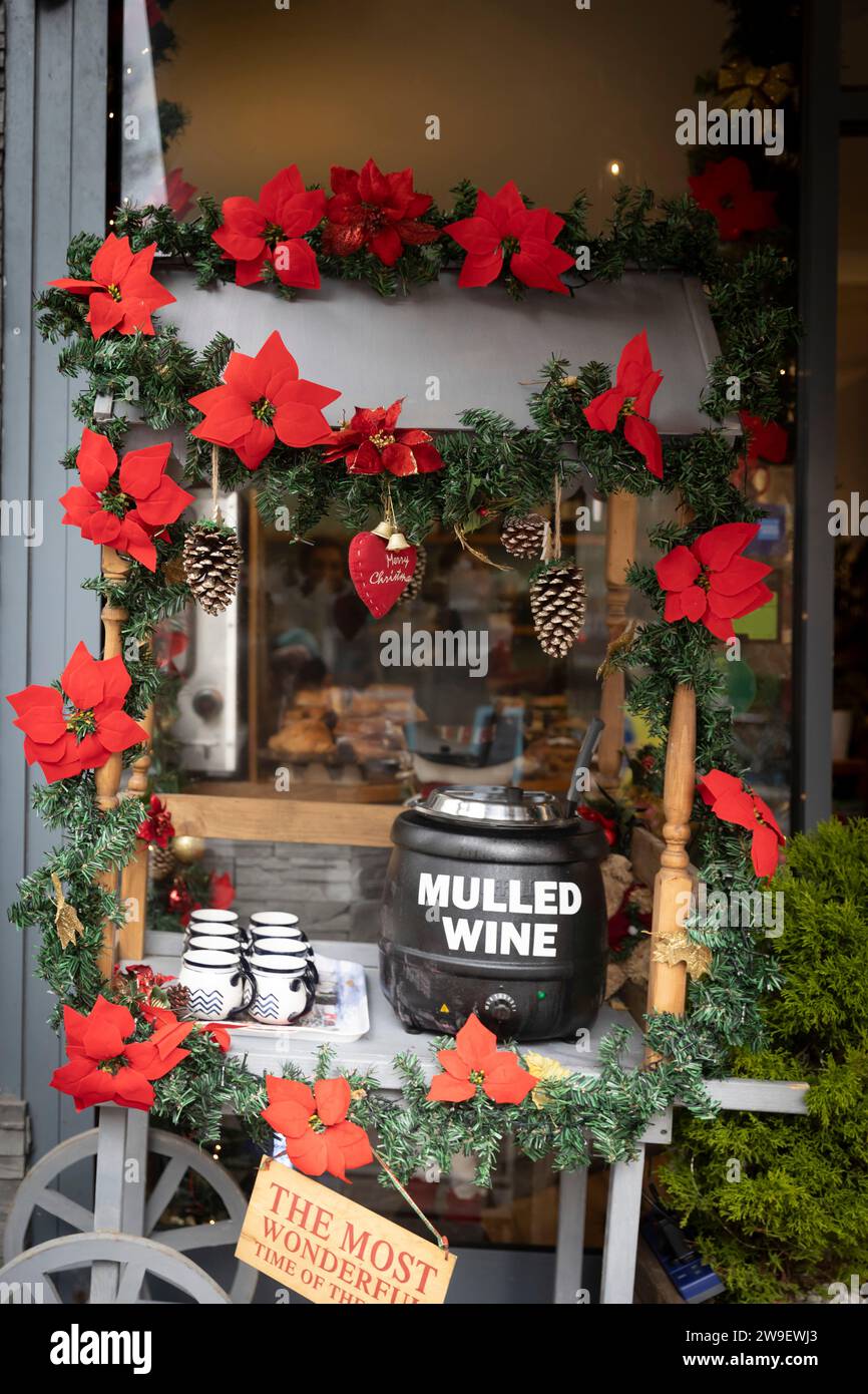 Table for selling mulled wine, decoration in the form of a poinsettia garland, cups for mulled wine. Christmas atmosphere in the cafe. Thermopot. Stock Photo