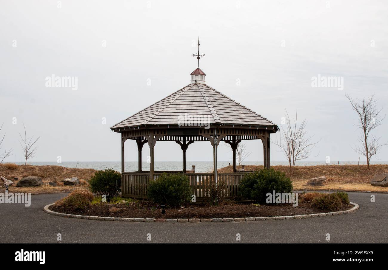 A wooden gazebo sitting on top of a lush green field at the end of a road by the water. Stock Photo