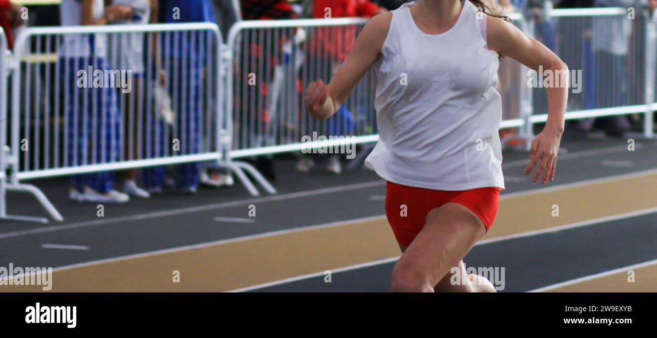 Front view of one teenage girls running in a track race on an indoor track. Stock Photo