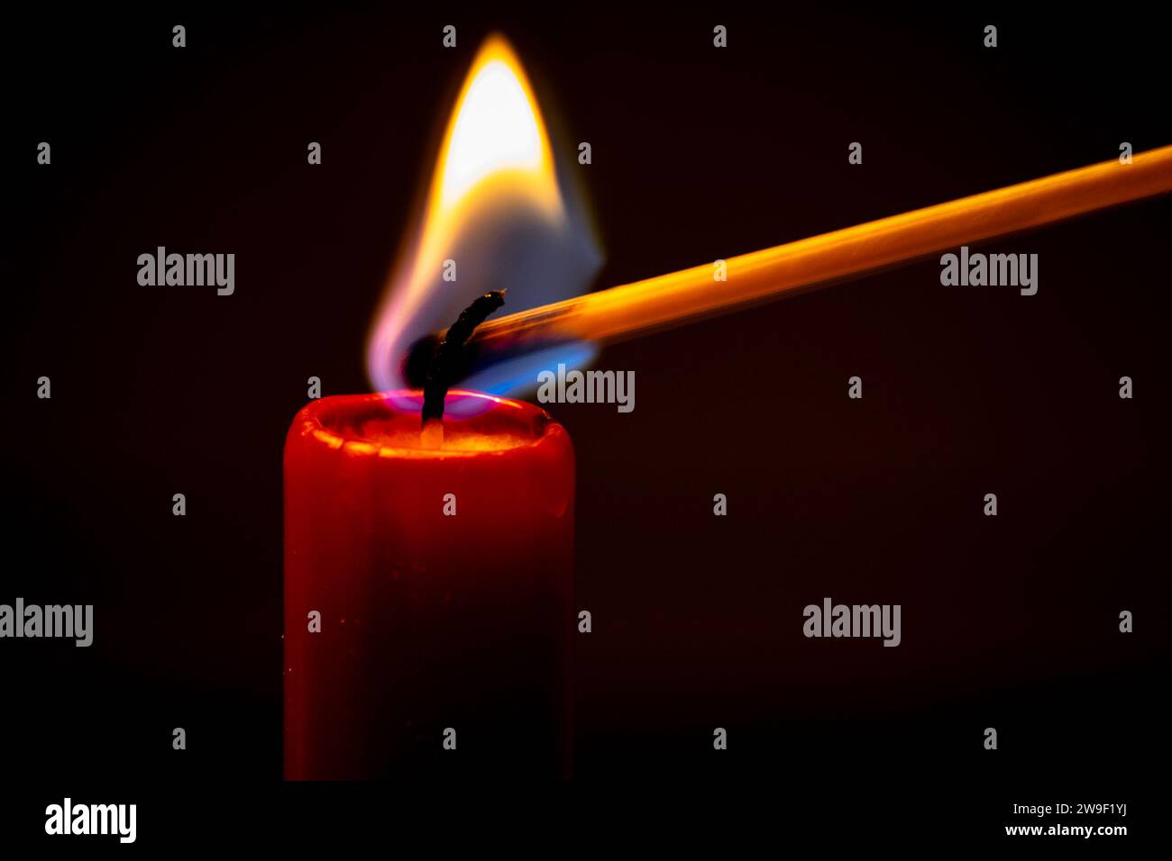 A red candle is lighted by a match. Stock Photo