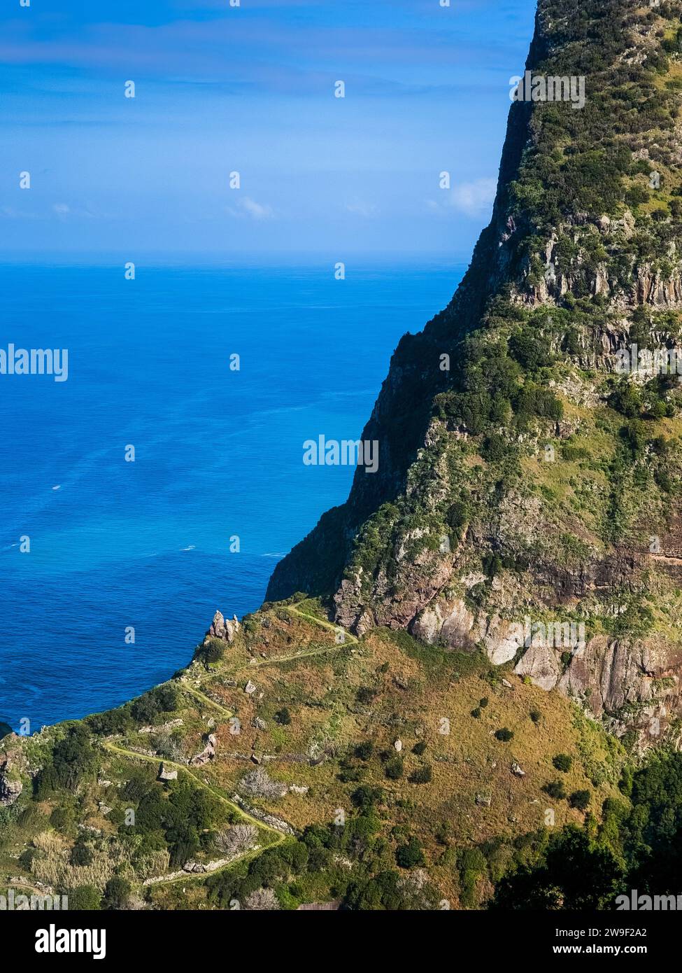 A stunning aerial view of a majestic mountain peak with its pointed spire, overlooking the tranquil blue ocean and lush green hills in the background Stock Photo