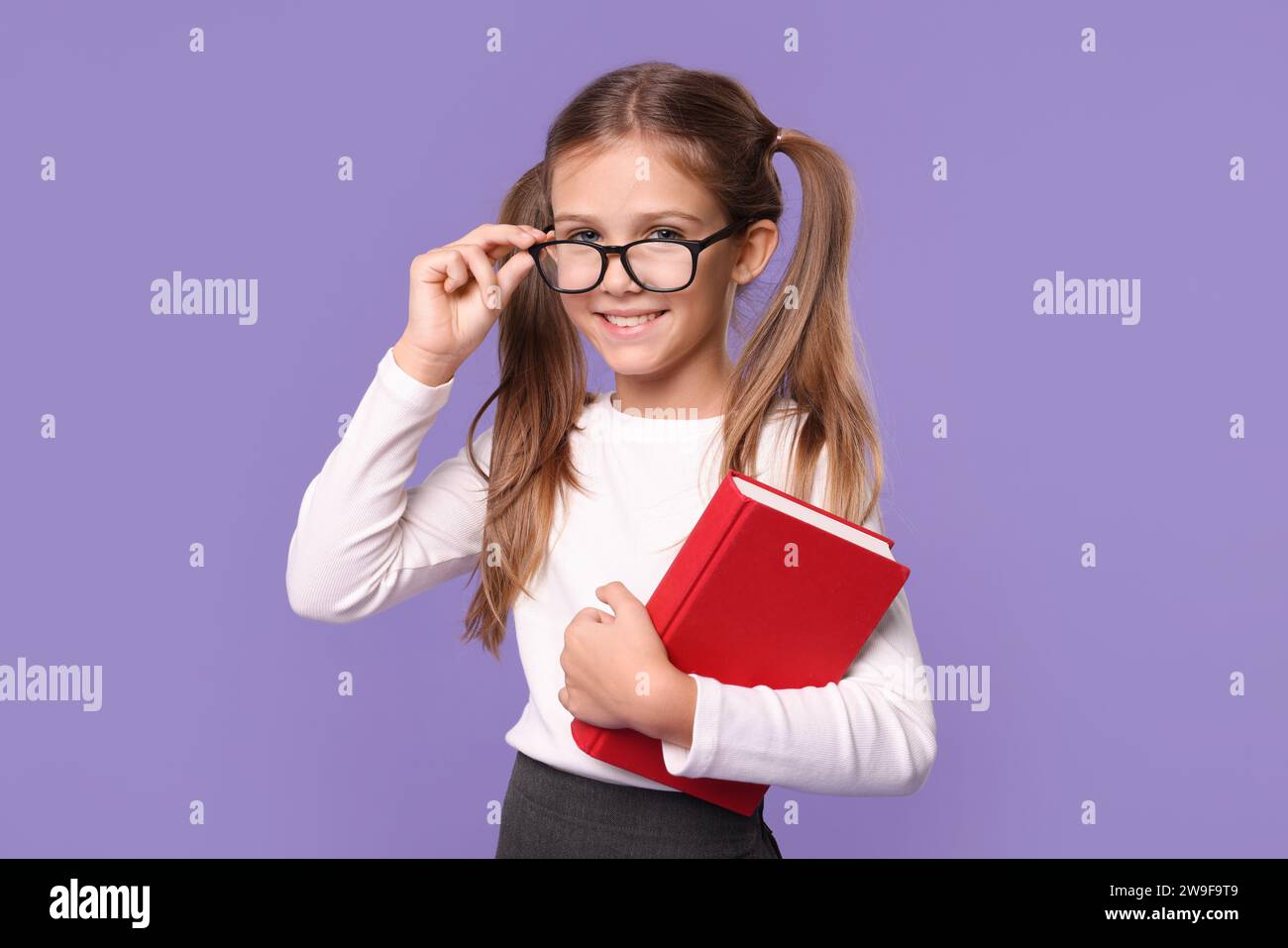 Smiling schoolgirl with book on violet background Stock Photo - Alamy