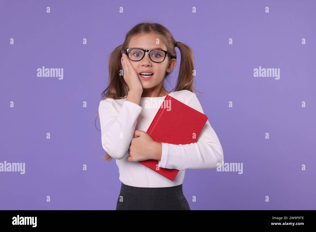 Excited schoolgirl with book on violet background Stock Photo - Alamy