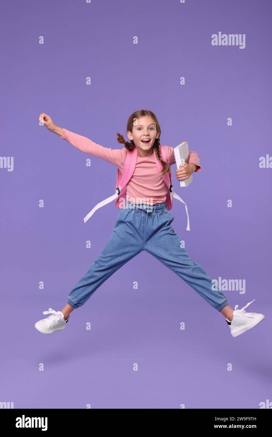 Happy schoolgirl with backpack jumping on violet background Stock Photo ...