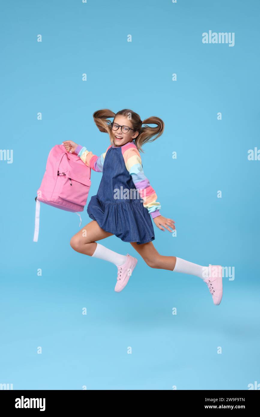 Happy schoolgirl with backpack jumping on light blue background Stock ...