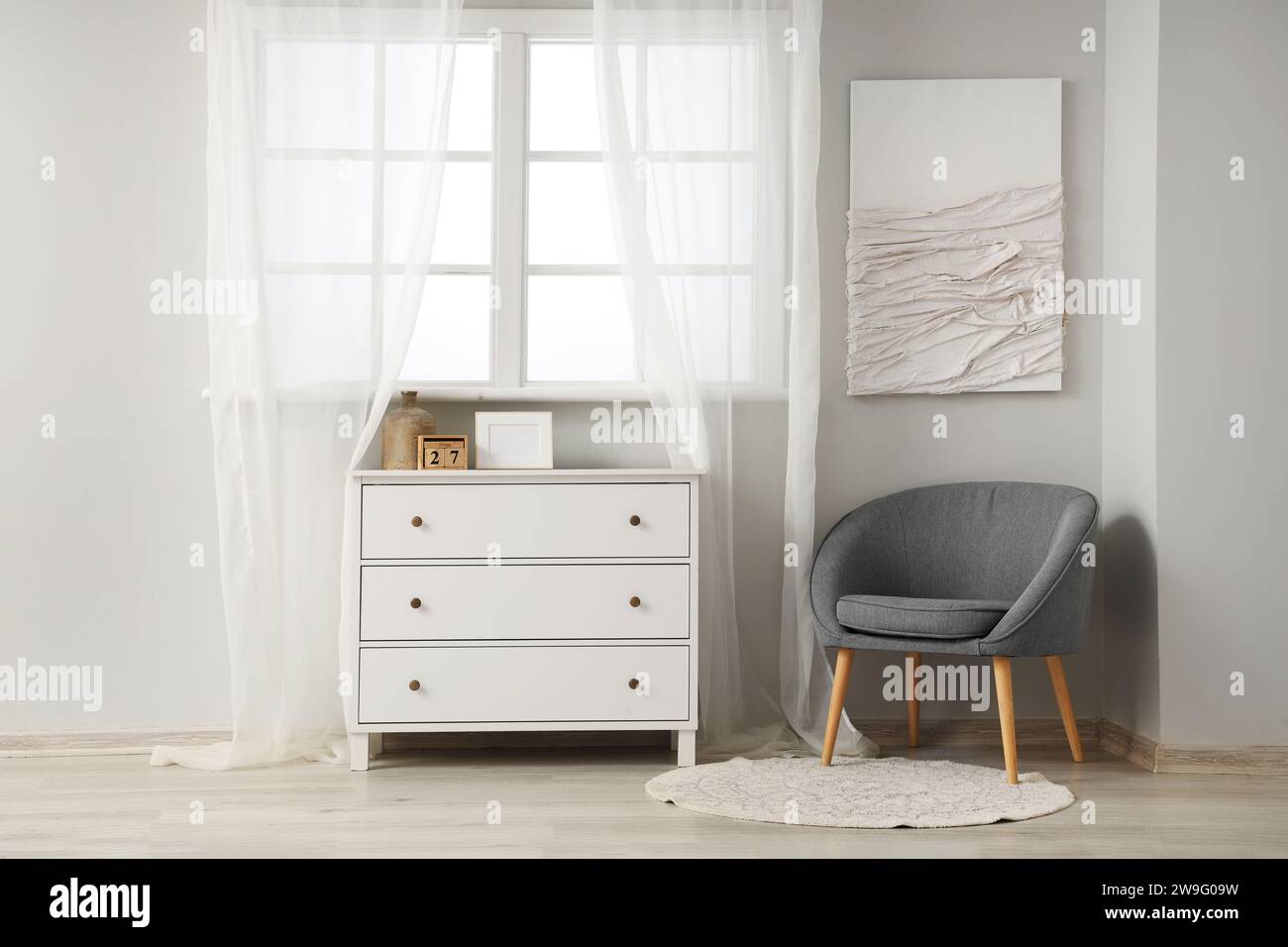 Interior of light living room with painting, grey armchair and chest of ...