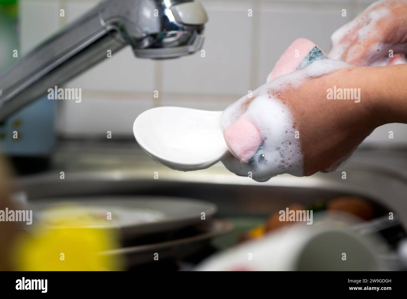 A hand with a dishwashing sponge washing the dishes and ladle Stock