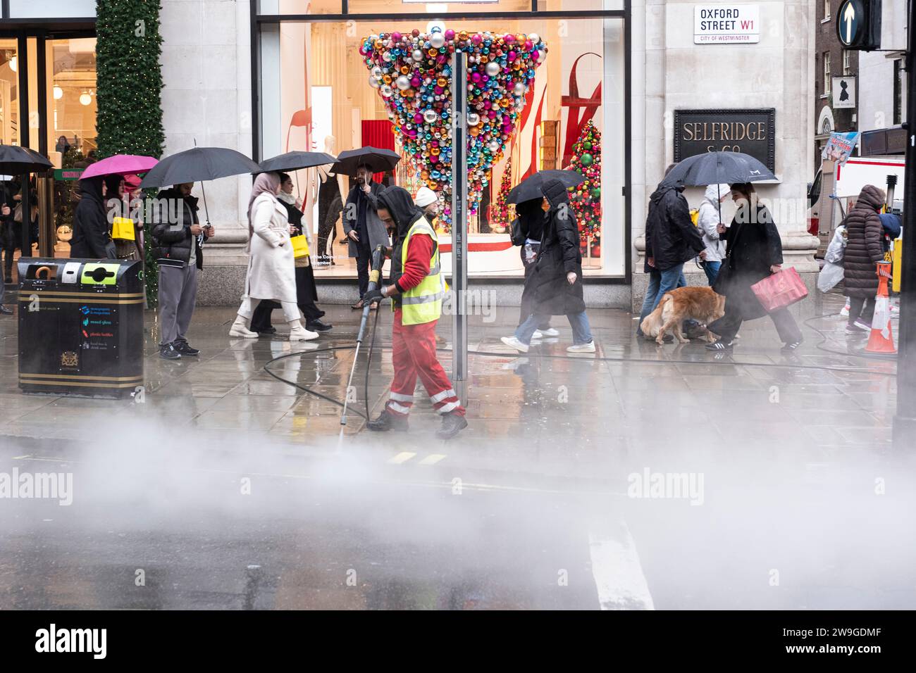 A cleaner, pressure steam cleaning the pavement in the rain with