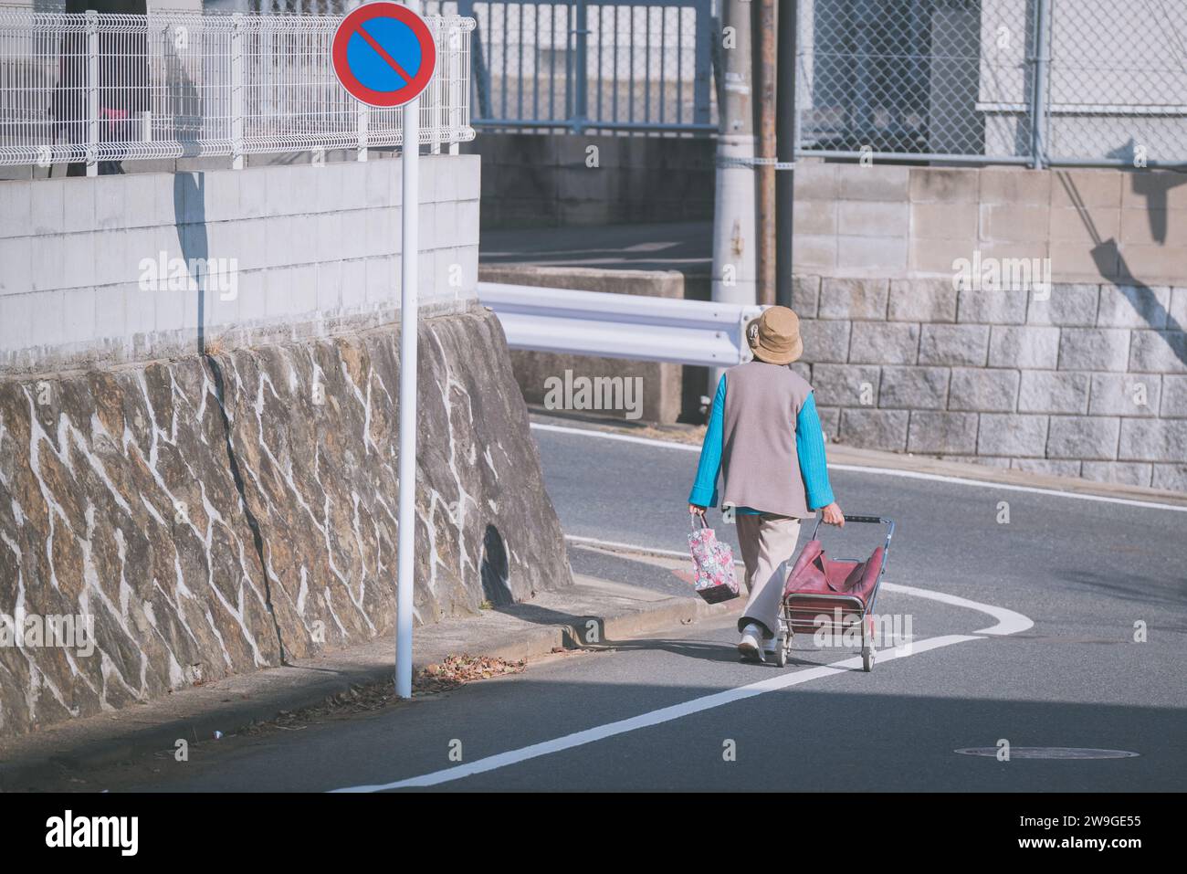 An old elderly Japanese woman walking and pulling her foldable shopping chair with wheels. Stock Photo