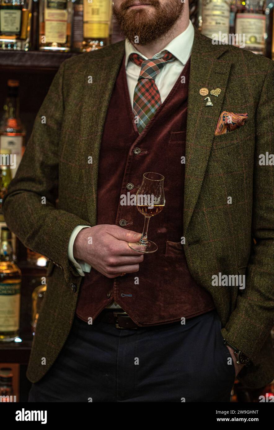 man holding a glass of scotch whisky wearing a suit standing in whisky , Scotland , UK . Stock Photo