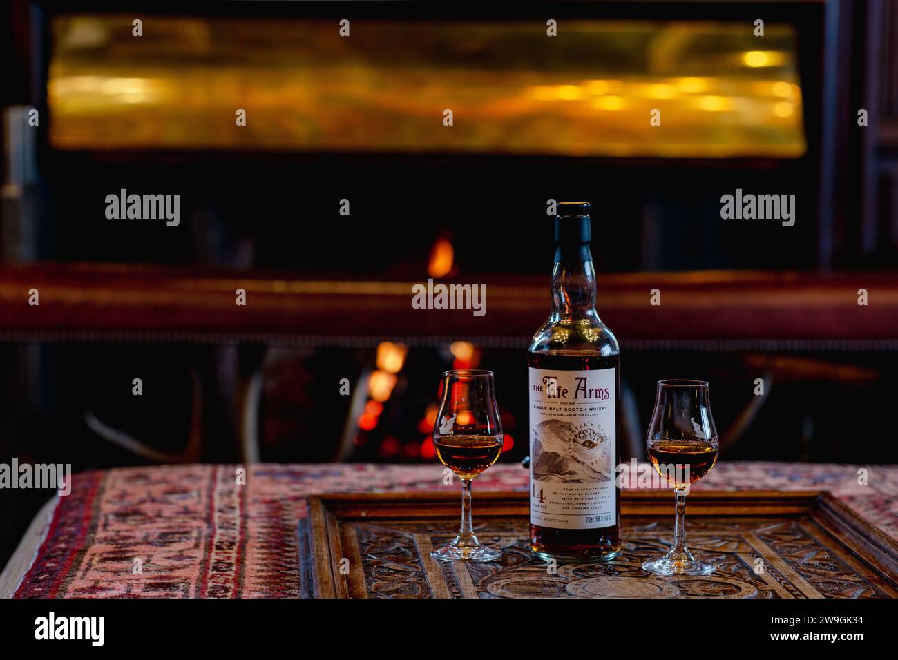Single malt whisky bottle with two glasses on the table near the burning fireplace. Rest and relaxation concept Stock Photo