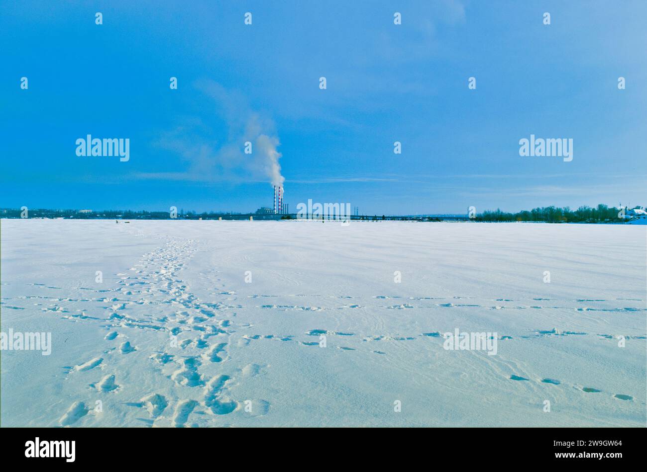 An old coal-fired power plant emission of toxic smoke into the atmosphere, industrial urban winter landscape with frozen river Stock Photo