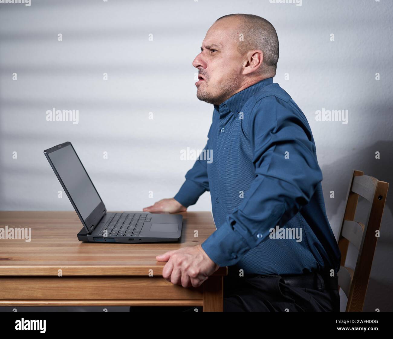 Mature business man sitting at his desk in front of his laptop, hostile, angry, threatening Stock Photo