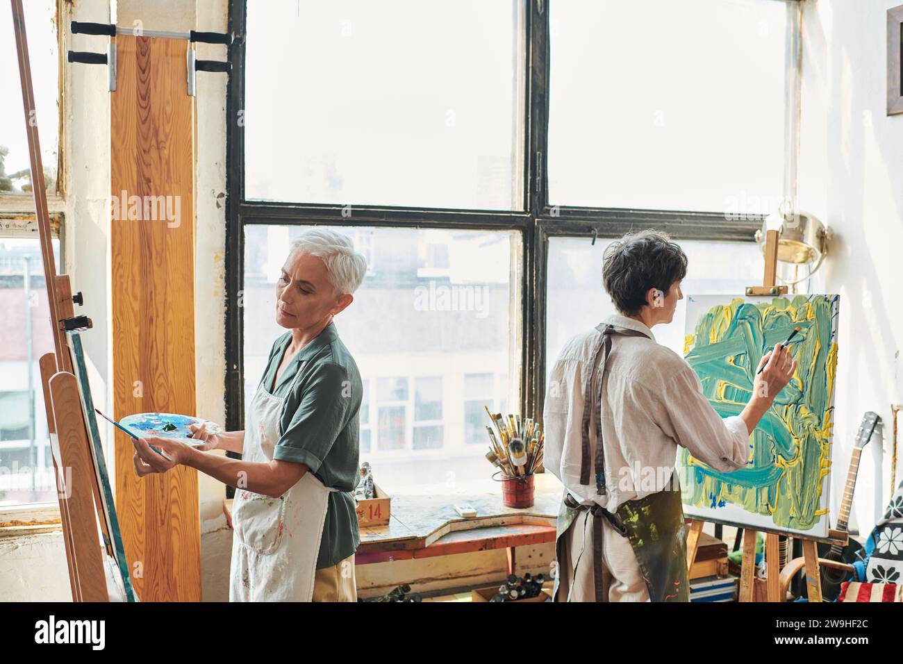 creative middle aged women in aprons painting on easels in modern craft